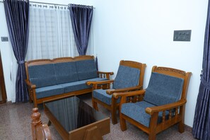 Una habitación con sofá, dos sillones, una mesa de centro de vidrio y cortinas.