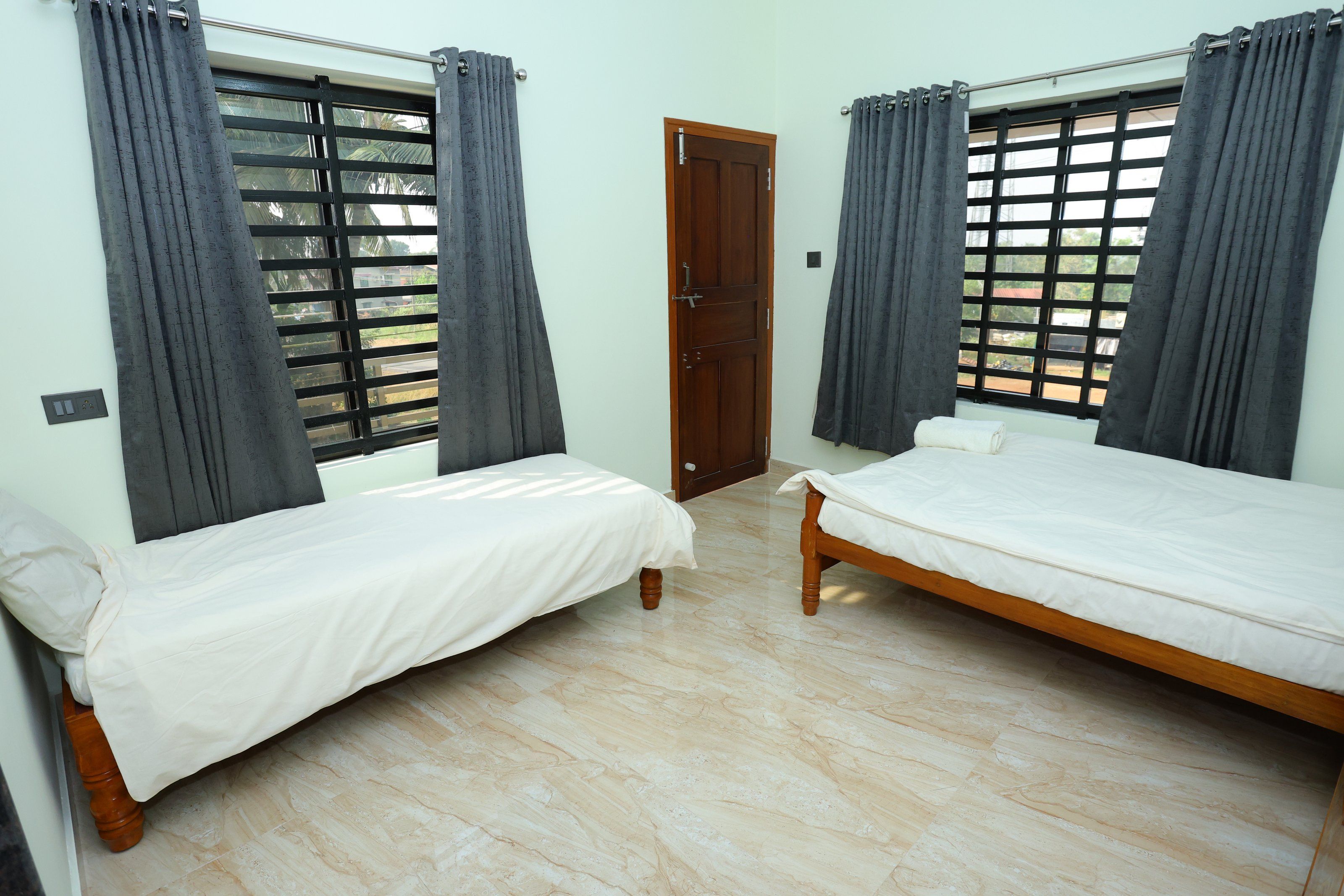 Una habitación con dos camas individuales, una puerta de madera y una ventana con diseño de celosía.