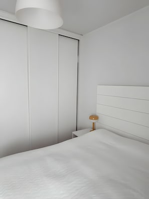 Een minimalistische slaapkamer met een bed, nachtkastje, lamp en een kledingkast.
