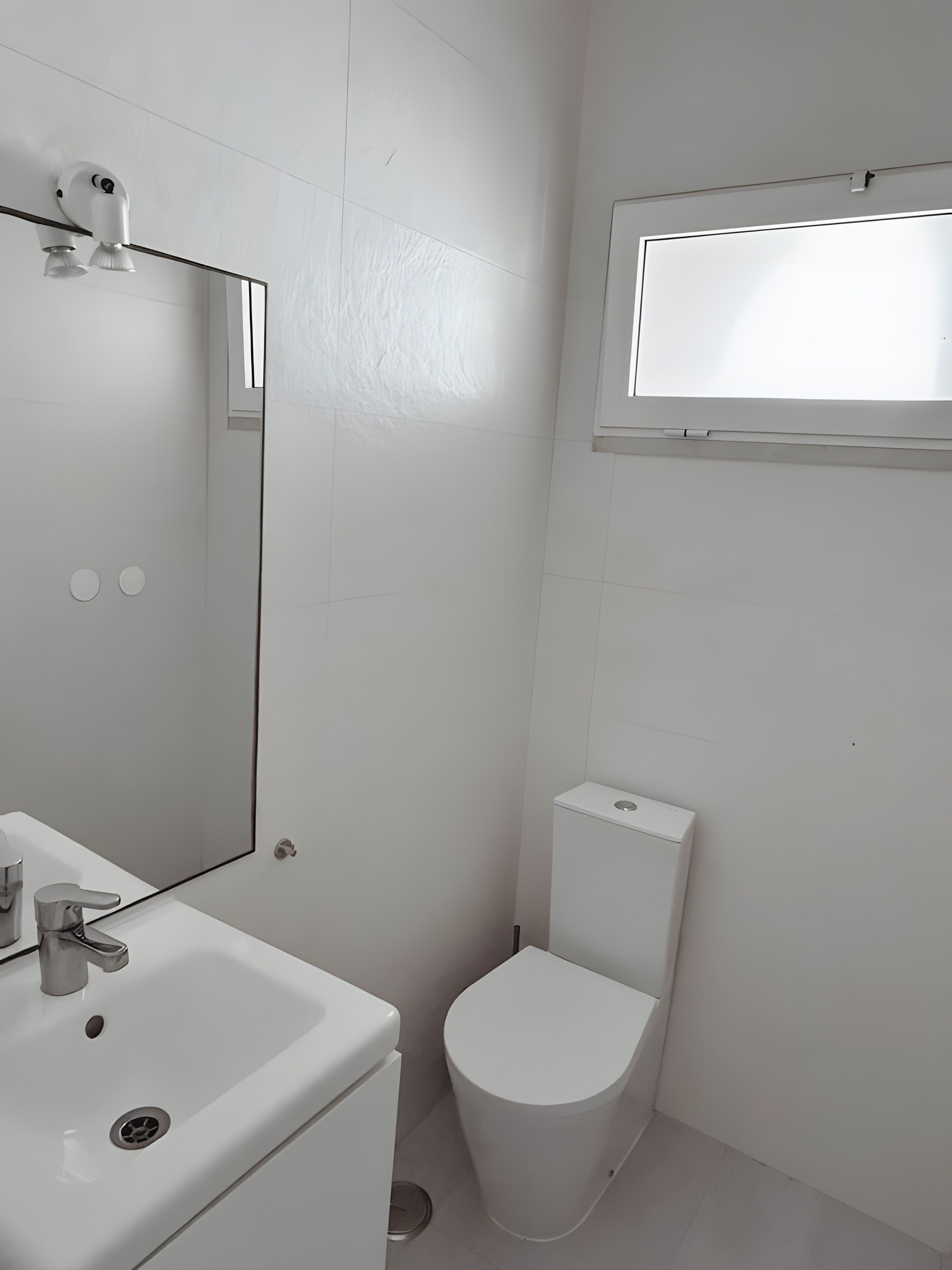 A bathroom with a white sink, mirror, toilet, and a window above the toilet.