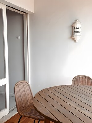 Quarto com mesa de madeira, cadeiras de vime, parede branca e um candeeiro branco.