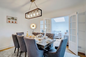 A dining area with a wooden table, grey upholstered chairs, and a hanging light fixture. - Norfolk Coast Beach House - Family & Dog Friendly - 4 Bed - Award Winning Luxury (Heacham)
