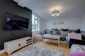 Una sala de estar moderna con una televisión de pantalla plana, un juego de sofá, una mesa de centro y una araña.