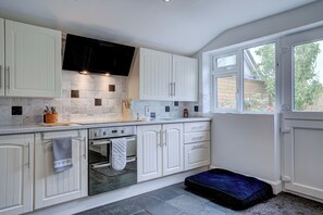 A modern kitchen with white cabinets, a black range hood, and a window providing natural light. - Norfolk Coast Beach House - Family & Dog Friendly - 4 Bed - Award Winning Luxury (Heacham)