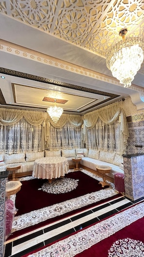A luxurious room with ornate ceiling patterns, a chandelier, and a plush seating area.