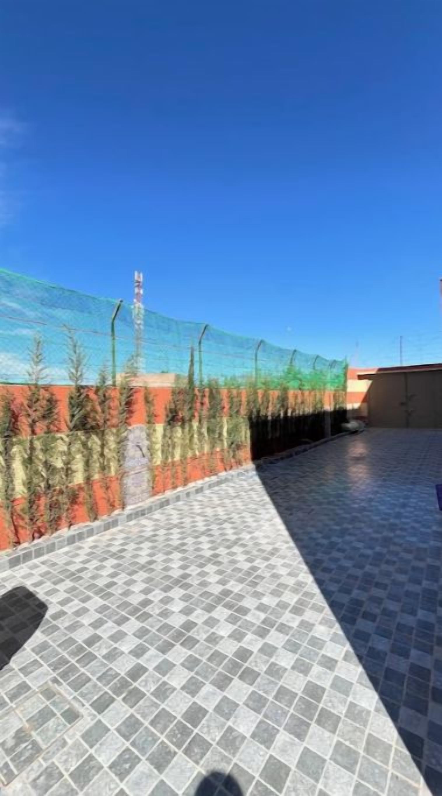 Una terrazza sul tetto con pavimento piastrellato, una zona protetta da una rete e cielo sereno.