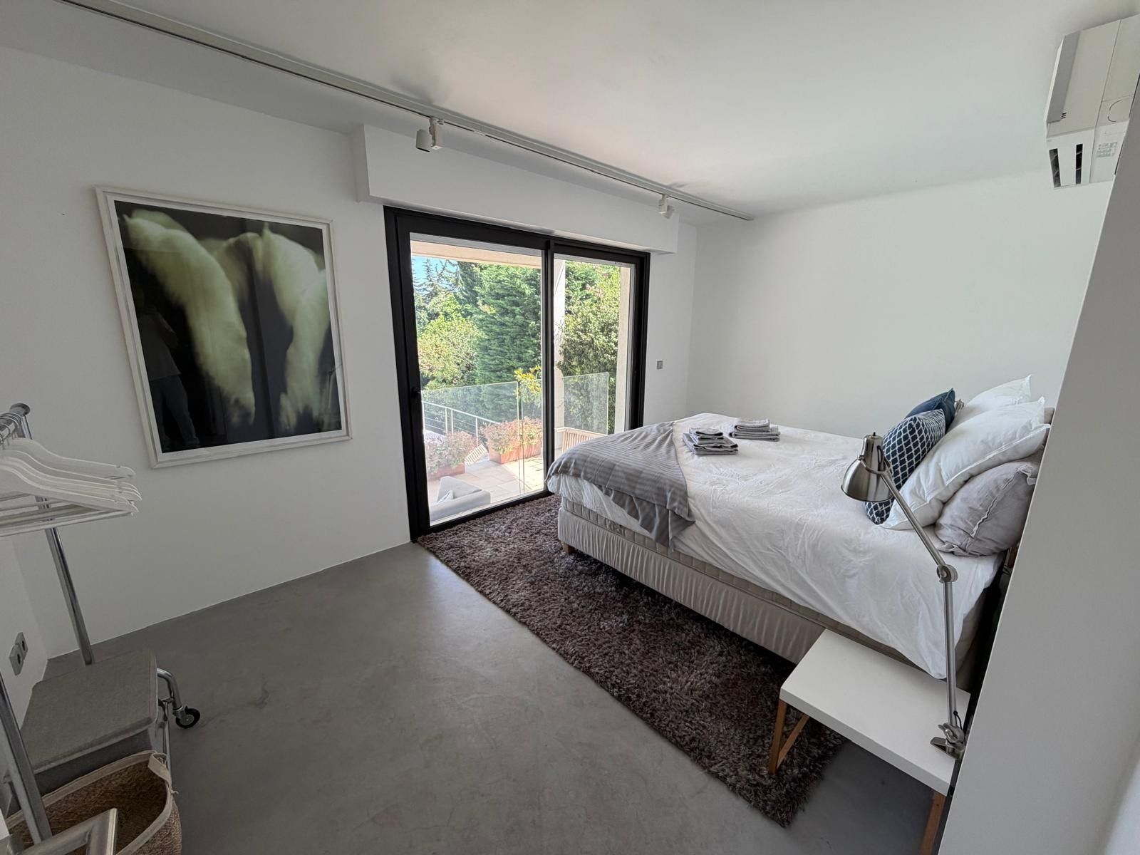 Een moderne slaapkamer met een groot bed, een nachtkastje, een stoel, een raam en een schilderij aan de muur.