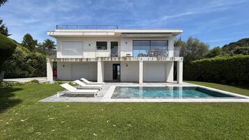 A modern two-story house with a swimming pool, a covered patio, and a well-maintained lawn.