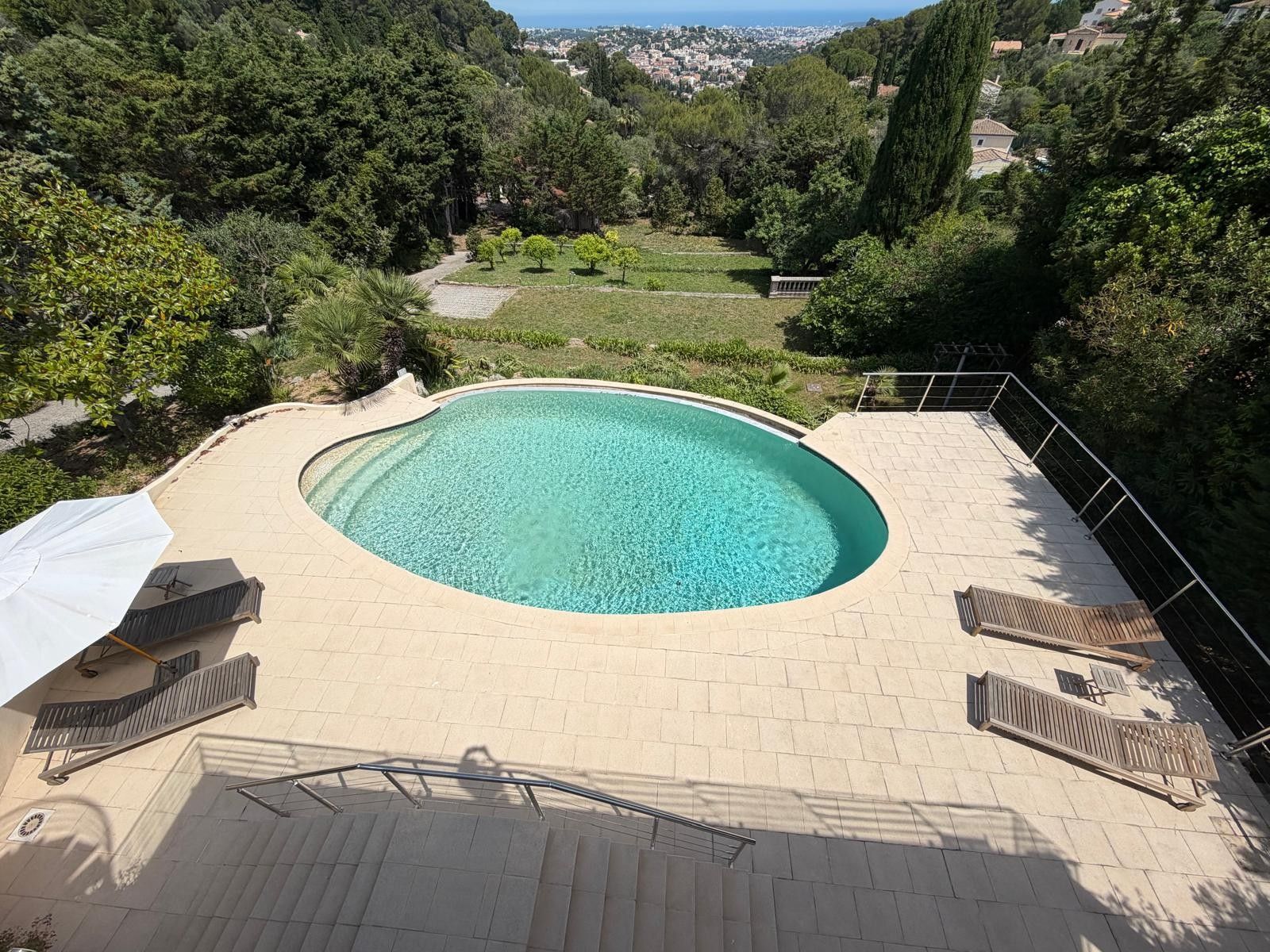 Una piscina a forma curva, circondata da un solarium piastrellato e un parapetto.