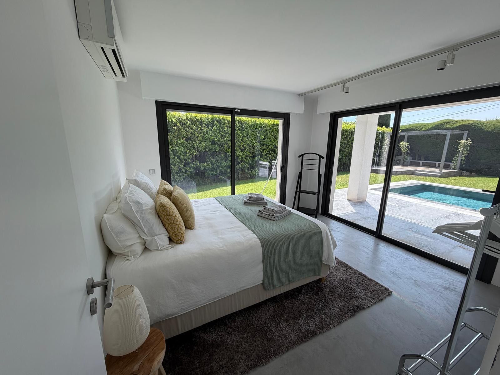 A bedroom with a large bed, a view of a swimming pool, and a sliding glass door leading to an outdoor area.