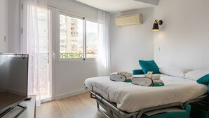 Una camera d'albergo con un letto, una TV, una finestra con tende, un condizionatore d'aria e un portalampada a parete.