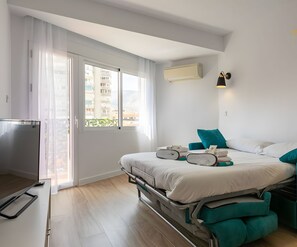 Een hotelkamer met een bed, een televisie, een raam met gordijnen, een airconditioning en een wandlamp.