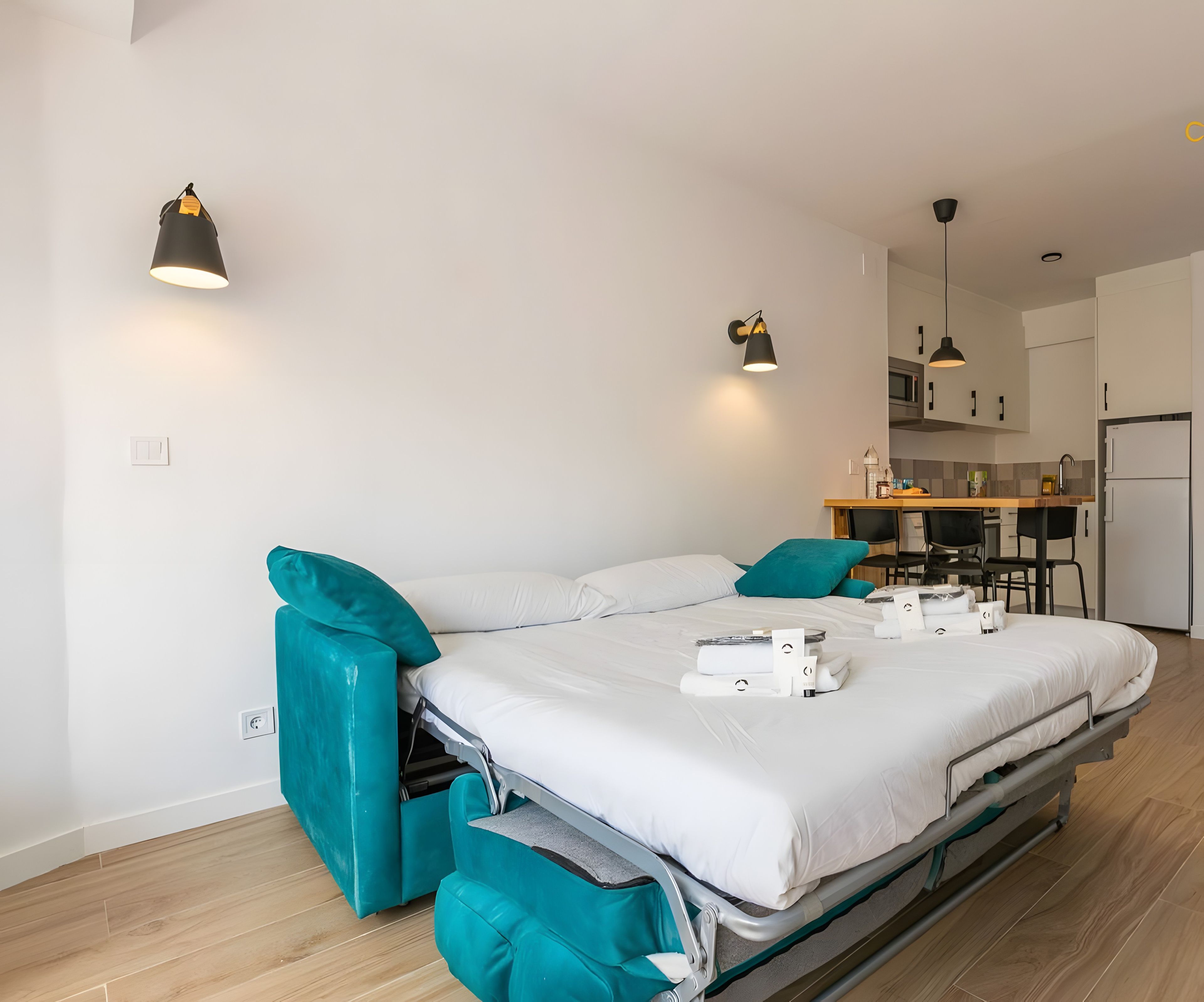 Quarto de hotel moderno com cama, cozinha compacta e banheiro.
