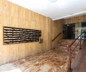 Pared de madera con un sistema de buzones metálicos, suelo de mármol y una escalera con barandillas de metal.