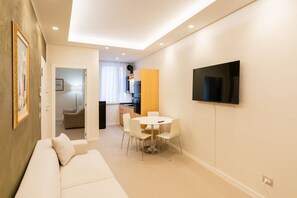 Un saló modern amb un sofà, una taula de dinar amb cadires, una zona de cuina i un televisió penjat.