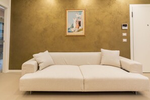 A beige sofa with pillows, a framed artwork on the wall, and a white door in a room with a textured wall. - Residenza De Nicolis - 50 meters from Piazza Erbe (Verona)
