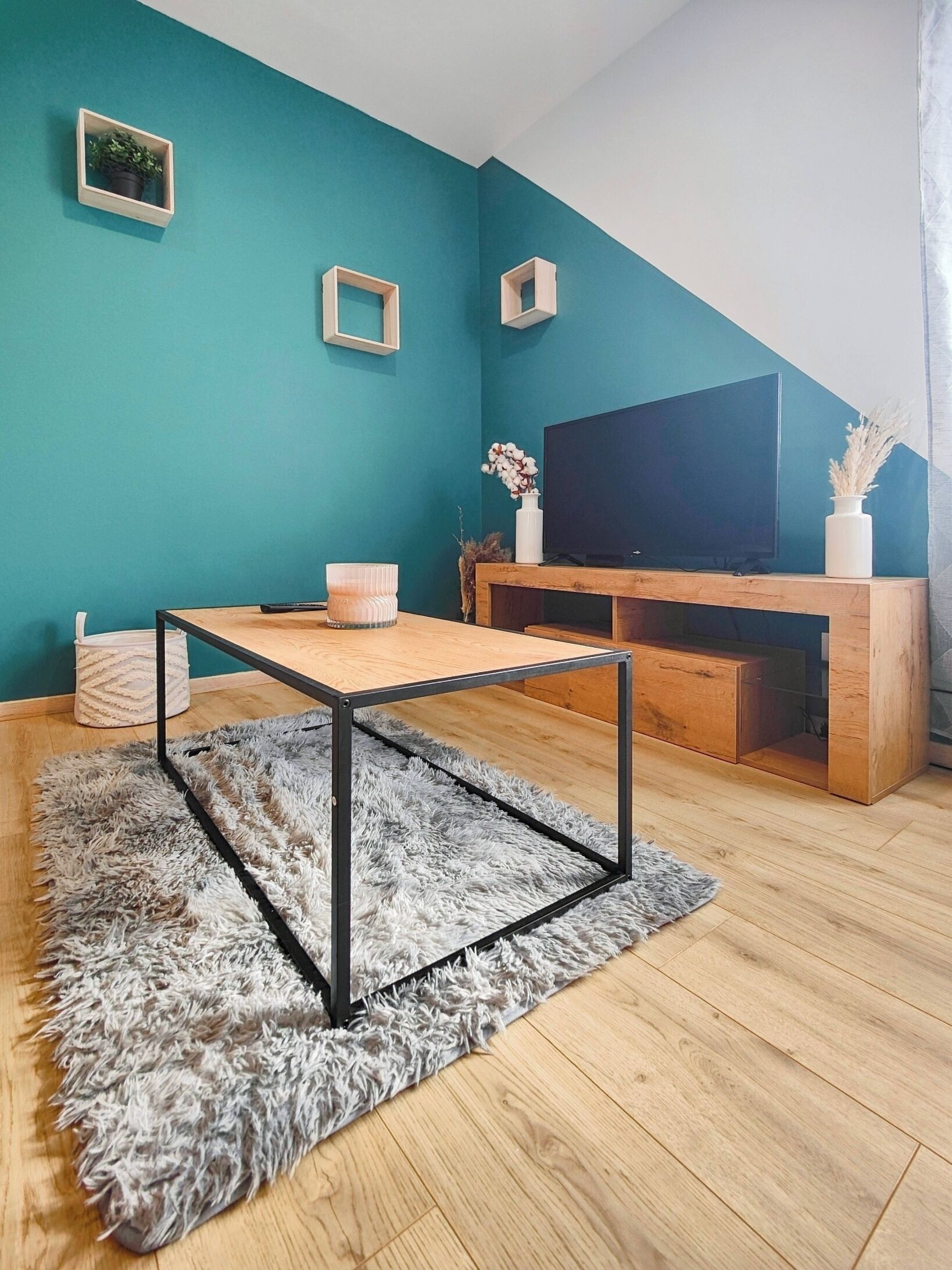 Een moderne woonkamer met teal muren, een houten salontafel, een zacht tapijt en een televisie op een houten dressoir.