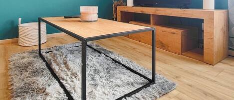 Een moderne woonkamer met teal muren, een houten salontafel, een zacht tapijt en een televisie op een houten dressoir.