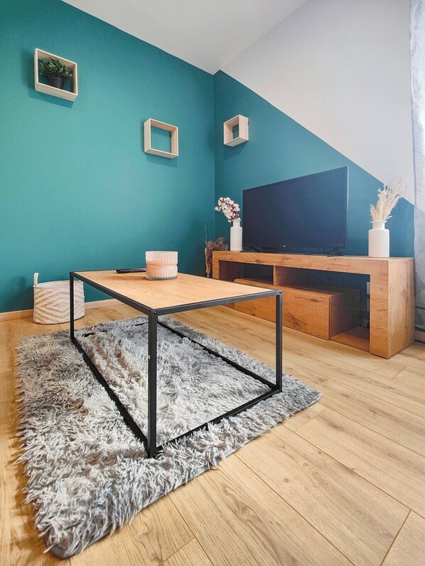 Una sala de estar moderna con paredes color turquesa, una mesa de centro de madera, una alfombra mullida y un televisor sobre un mueble de madera.