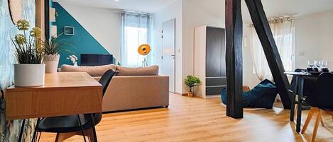 A modern living room with a wooden floor, a sofa, a dining table, and a staircase.