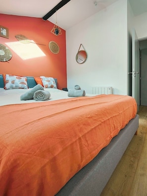 Un dormitorio moderno con una cama grande, ropa de cama naranja y un radiador blanco.