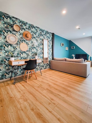 Una habitación con escritorio, una silla, un sofá y una pared con un diseño de hojas.