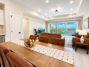 A modern living room with a wooden dining table, leather sofas, and a view of a mountainous landscape through large sliding doors. - Brand New Condo Steps to Lumberjack Square | Mt. LeConte View (Pigeon Forge)