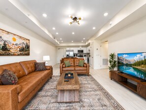 A modern living room with a brown leather sofa, a wooden coffee table, and a large flat-screen TV on a wooden stand. - Brand New Condo Steps to Lumberjack Square | Mt. LeConte View (Pigeon Forge)