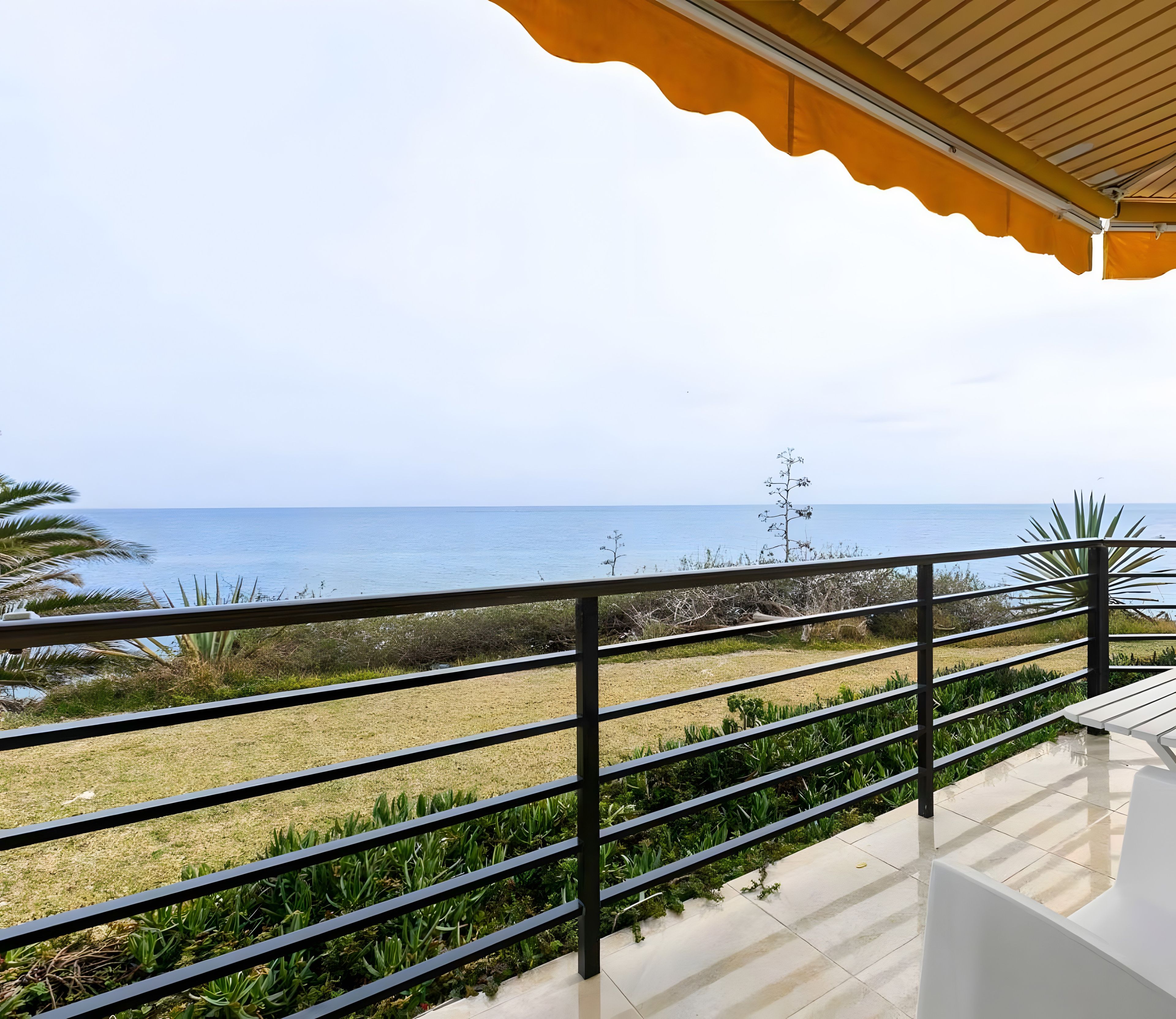 A balcony with a view of the sea, a railing, and a tiled floor.