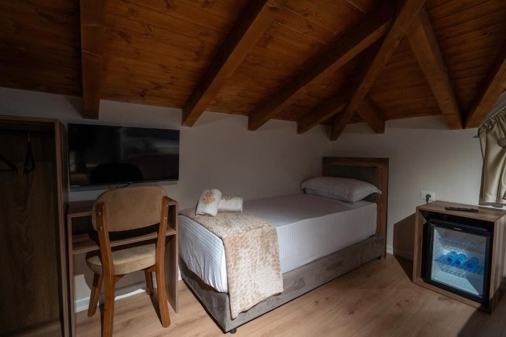 A bedroom with a bed, a chair, a small refrigerator, and a window.