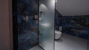 Een moderne badkamer met een glazen douchewand, een wit toilet en een marmeren wand.