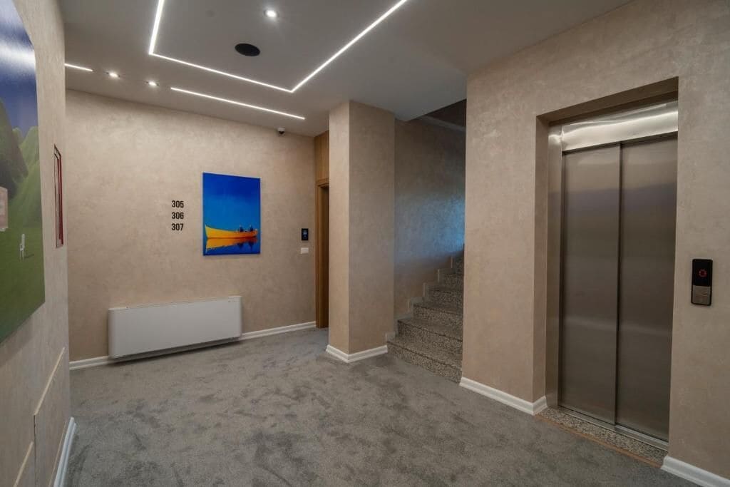 A hallway with a carpeted floor, a painting on the wall, and an elevator.