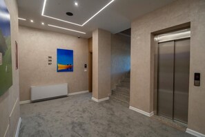 Un pasillo con piso alfombrado, un cuadro en la pared y un ascensor.