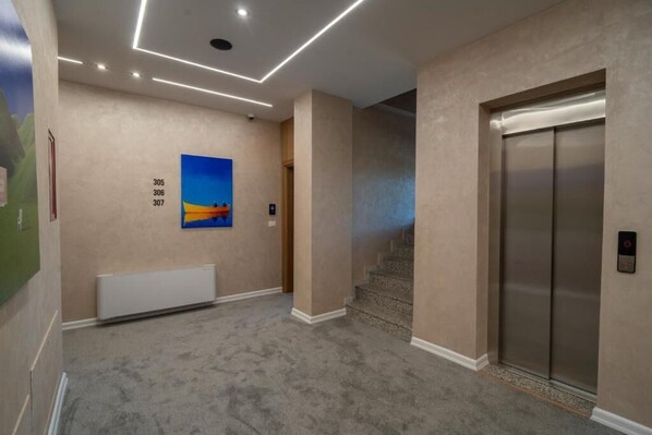 A hallway with a carpeted floor, a painting on the wall, and an elevator.