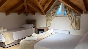 Quarto com duas camas, vigas de madeira no teto, uma janela com cortinas e uma mesa de cabeceira com abajur.