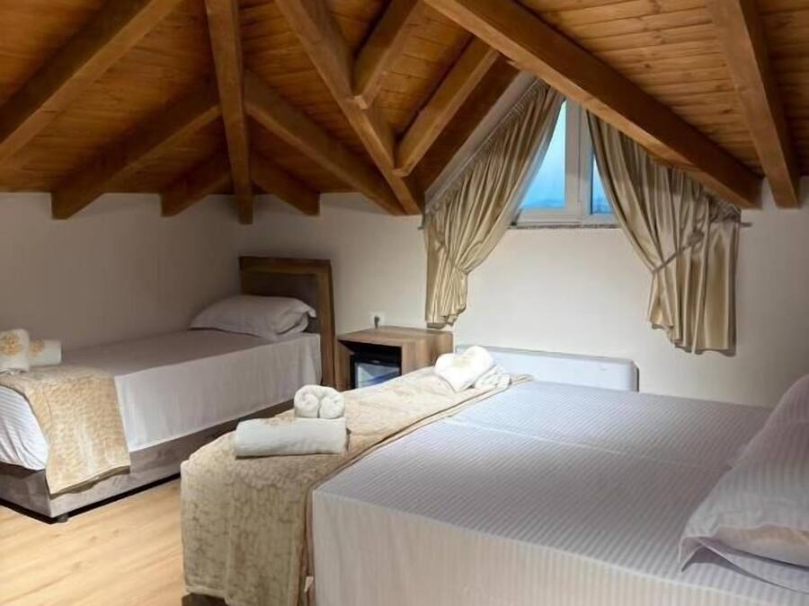 Un dormitorio con dos camas, vigas de madera en el techo, una ventana con cortinas y una mesita de noche con lámpara.