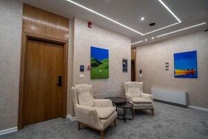 A hotel lobby with two armchairs, a small table, and artwork on the walls.