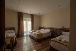 A hotel room with two beds, a wooden floor, and a large window with curtains.