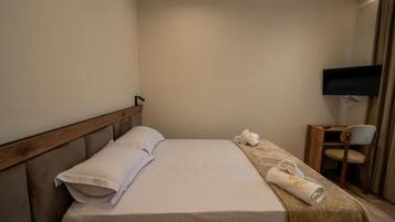 A hotel room with a bed, a TV mounted on the wall, a chair, and a wooden nightstand.