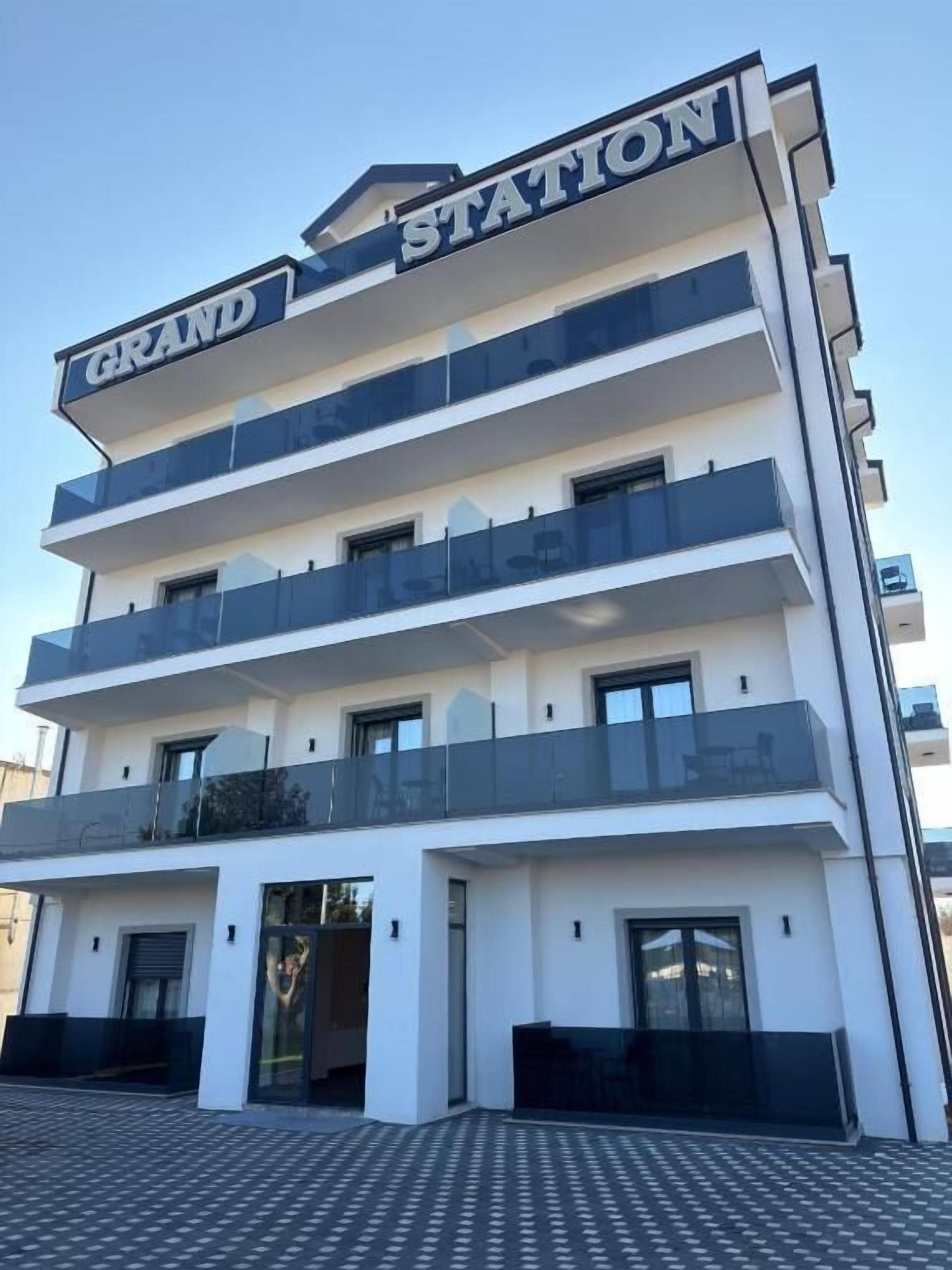 A multi-story hotel with a prominent 'GRAND STATION' sign, balconies on each floor, and a patterned ground floor.