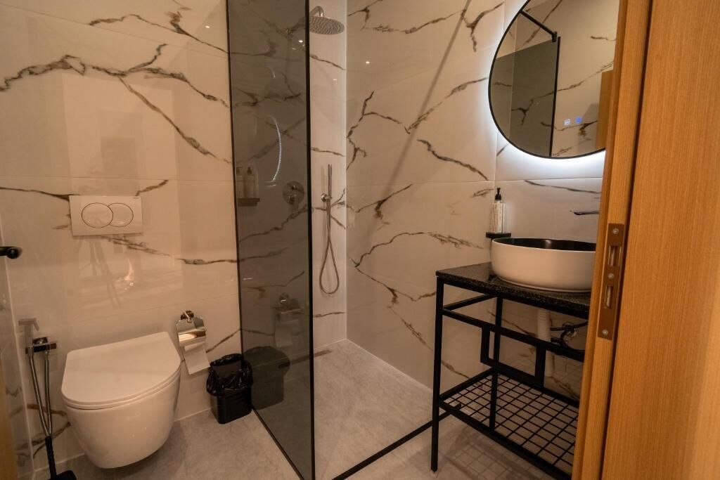 A modern bathroom with a toilet, a glass-enclosed shower, and a sink with a marble backsplash.