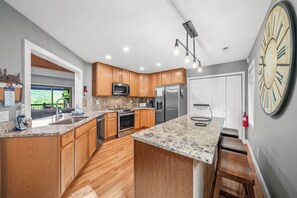 Una cocina moderna con armarios de madera, electrodomésticos de acero inoxidable, encimeras de granito y un reloj de pared grande.