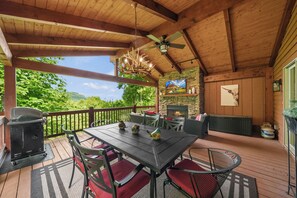 Eine überdachte Terrasse im Freien mit Esstisch, Stühlen, Grill und Kamin.