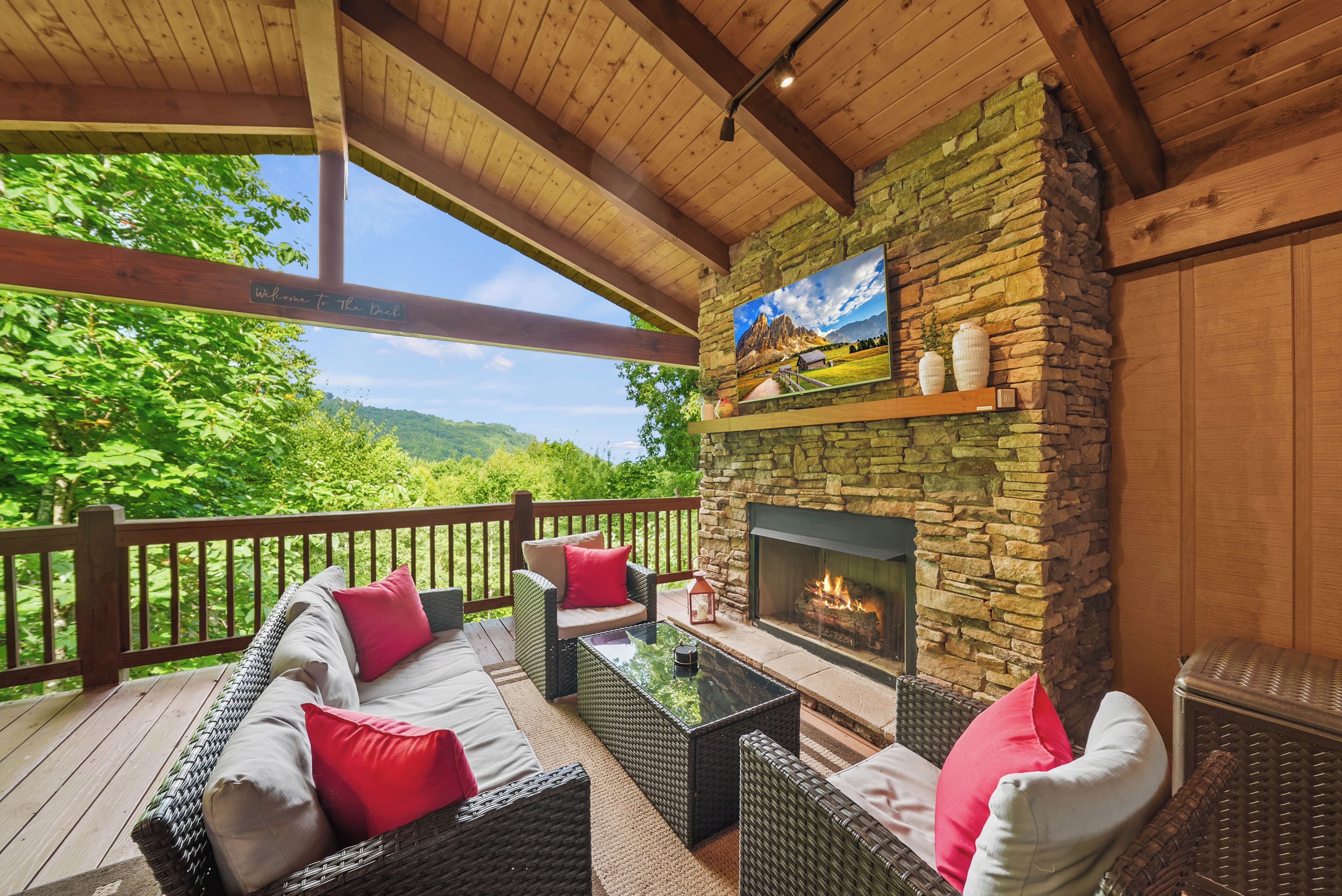 A covered outdoor seating area with wicker furniture, a stone fireplace, and a scenic view.