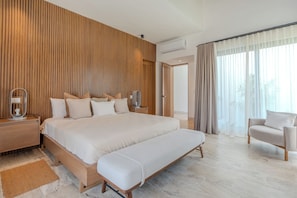 Ein modernes Hotelzimmer mit einem großen Bett, Nachttischen, einer Bank, einem Sessel und Blick ins Freie durch transparente Vorhänge.