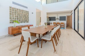 Ein moderner Essbereich mit einem langen Holztisch und passenden Stühlen, einer dekorativen Wand und einer Küche im Hintergrund.