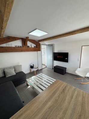 Een moderne woonkamer met een bank, een salontafel, een televisie en een houten balk in het plafond.