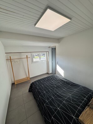 A bedroom with a bed, a wooden drying rack, a window, and a door. - Vacation Rental in the Heart of the Ardèche (Beaulieu)