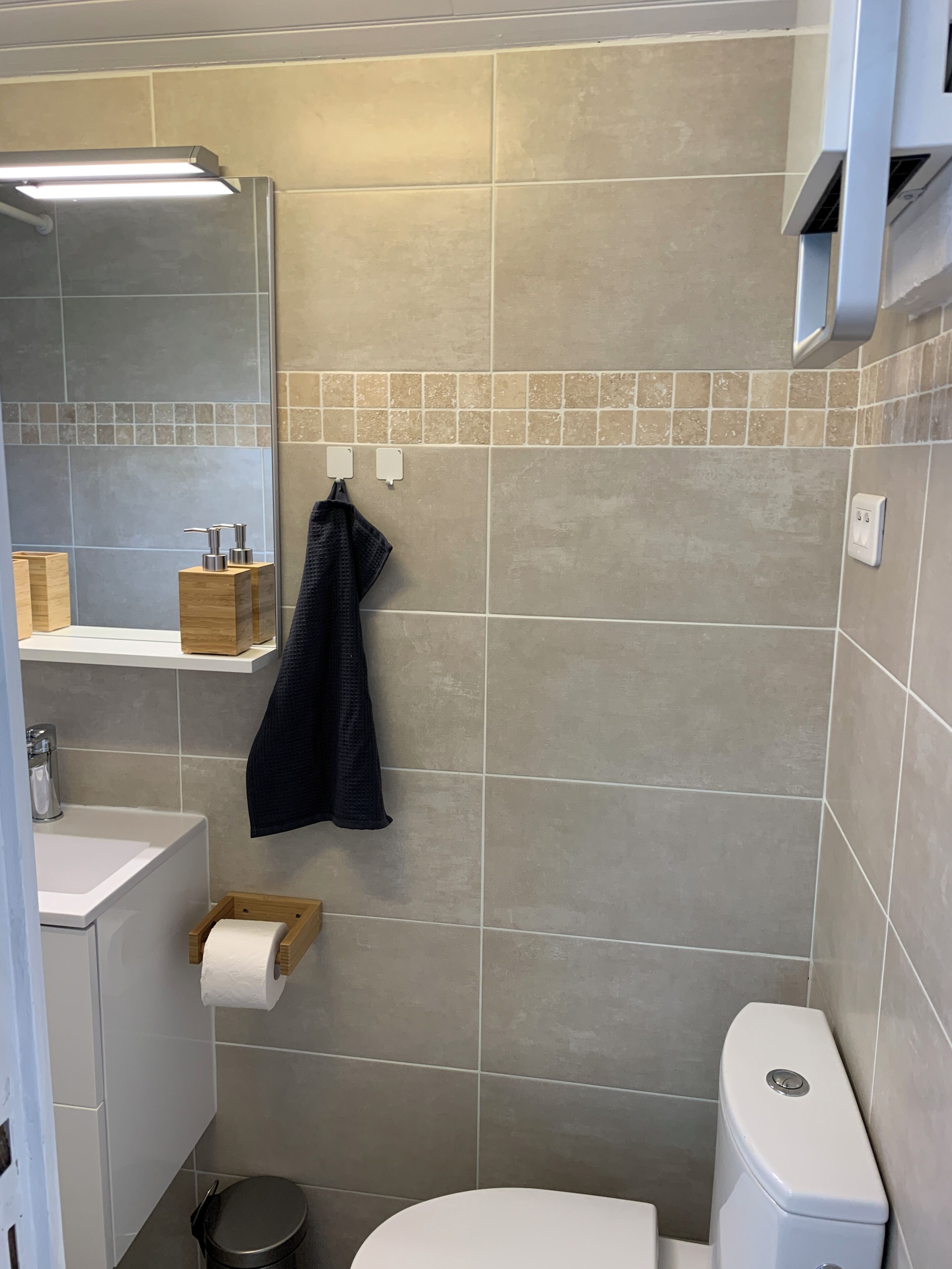 A bathroom with a toilet, sink, mirror, towel rack, and a trash bin.