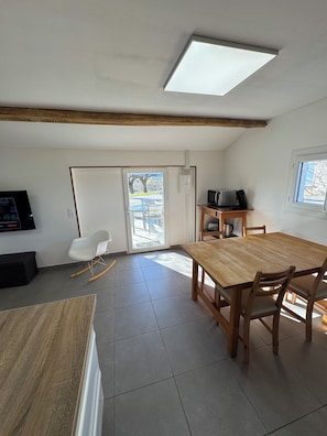 A room with a wooden dining table, chairs, a television, and a kitchen area with a microwave. - Vacation Rental in the Heart of the Ardèche (Beaulieu)